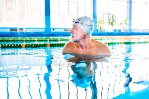 Senior man in water in an indoor swimming pool. Active pensioner enjoying sport.